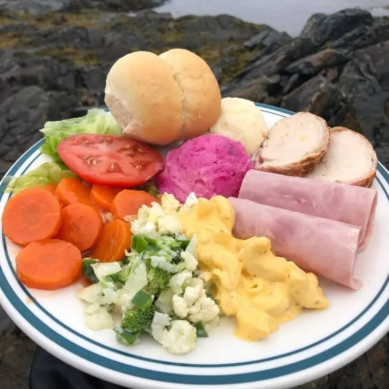 A cold plate with a roll, ham, chicken, salad and vegetables