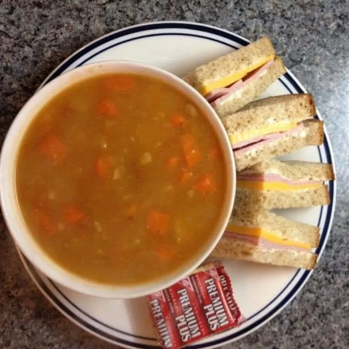 A bowl of vegetable beef soup with small sandwiches